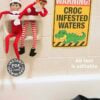 The Christmas Elf Croc Warning Sign Bathtub Prank features two toy elves on a soap dish above a "Warning! Croc Infested Waters" sign with a cartoon crocodile, plus Crocs shoes by the tub for a playful, humorous touch.