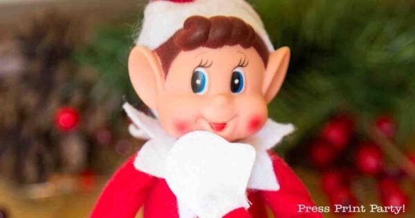 A smiling Elf on the Shelf doll dressed in red and white sits in front of a blurred festive background with greenery and red berries, surrounded by fun printable Elf on the Shelf props. The words "Press Print Party!" appear in the lower right corner.