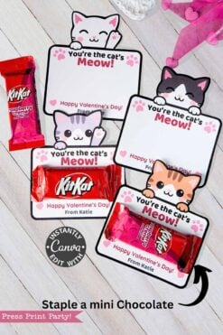 Cat Valentine Cards Printable for KitKat are shown—three cards featuring “You’re the cat’s meow!” paired with KitKat bars—displayed on a light wooden surface with pink heart decorations.