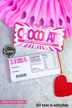 A Valentine’s Day chocolate bar with a pink and white wrapper sits on a card with custom text, next to the Valentines Day Socks Wrap Printable, another Choceur dark chocolate bar, and a crocheted heart.