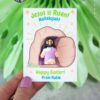 A hand holds the "Jesus Is Risen Easter Card for Mini Figurine," featuring a cartoon Jesus by an empty tomb. The card shows editable text: “Jesus is Risen! Hallelujah! Happy Easter! From Katie.” Green leaves decorate the background.