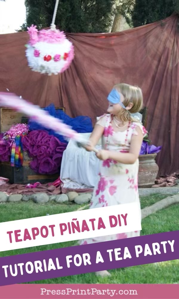 A young girl in a floral dress and blindfold swings a bat at a teapot-shaped piñata at an outdoor tea party, with colorful decorations and draped fabric in the background. Text reads: "Teapot Piñata DIY Tutorial for a Tea Party.