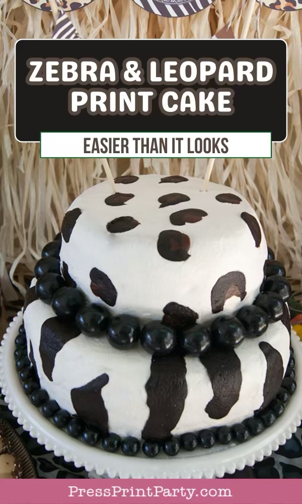 A two-tier cake decorated with white icing and zebra and leopard print patterns, topped and bordered with black candies. A sign above reads "Zebra & Leopard Print Cake - Easier Than It Looks.