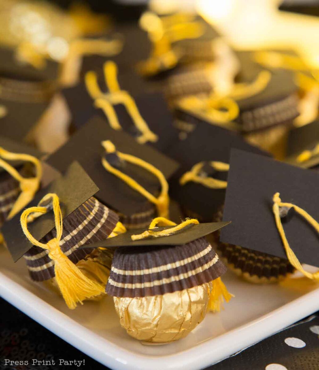 A tray of gold-wrapped chocolates decorated with black paper graduation caps and yellow tassels, arranged neatly as festive treats for a graduation celebration.