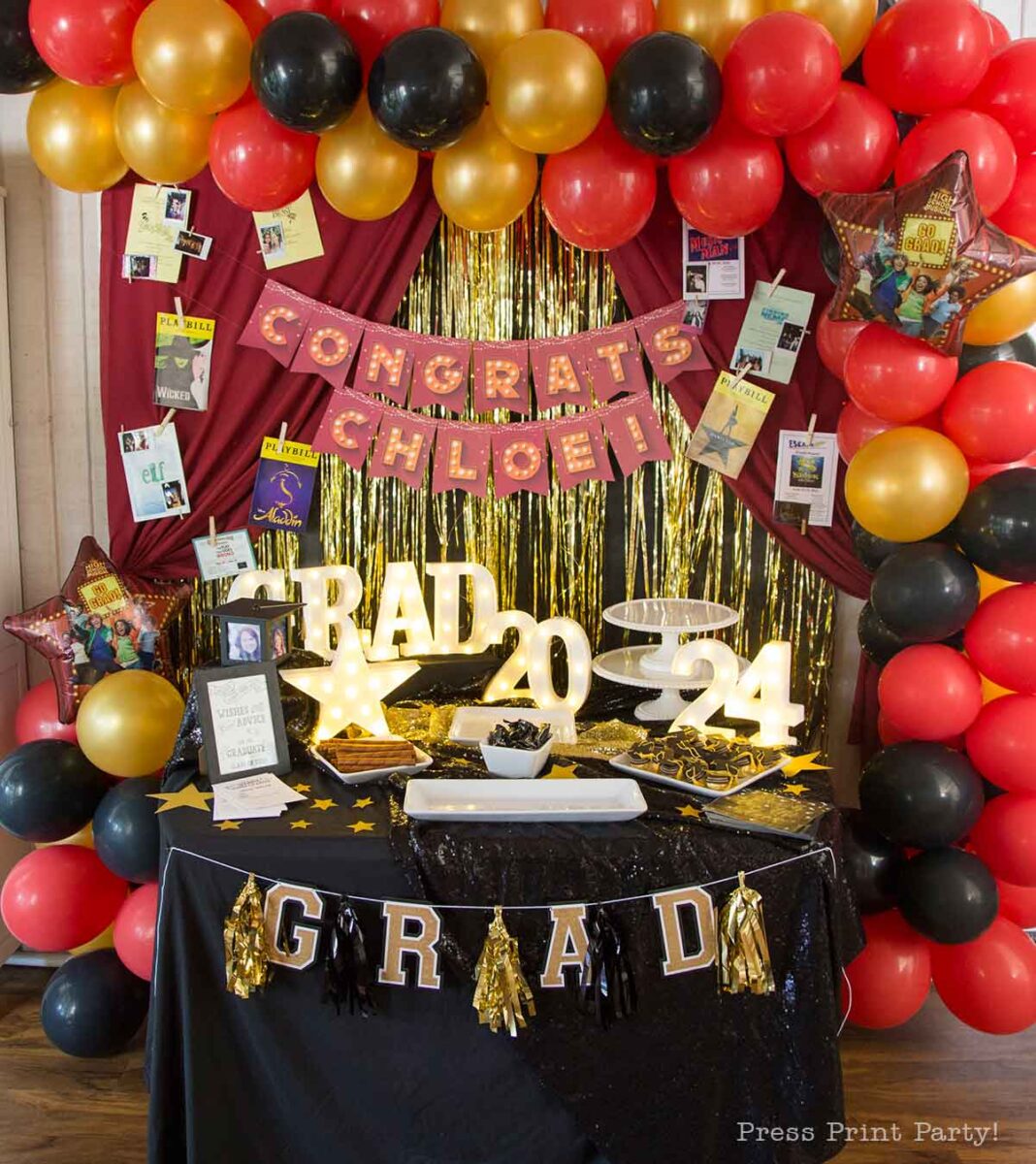 Colorful theater themed graduation party setup with red, gold, and black balloons, a βCongrats Chloe!β banner, gold fringe backdrop, photos, βRAD 2024β light-up letters, and a table decorated with a βGRADβ banner and stars.