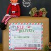 A wrapped gift sits on a table, topped with a small elf doll and festive decor, featuring the 2 Elves Arrival Postcard Printable as an editable delivery label. Text notes that the label can be customized using Canva.