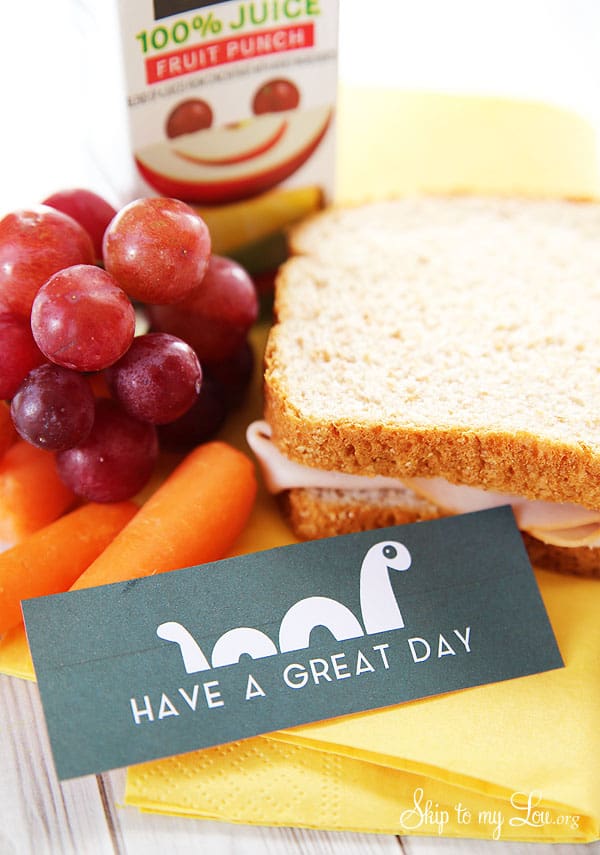 A turkey sandwich, baby carrots, grapes, and a juice box are arranged with a cute dinosaur-themed note that says “Have a great day.”.