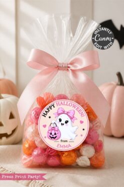 Clear bag of pink, orange, and white candies tied with a pink ribbon, featuring a “Happy Halloween” label from our 6 Pink Coquette Halloween Ghost Round Labels set, adorned with a cute ghost and pumpkin. White and pink pumpkins are in the blurred background.