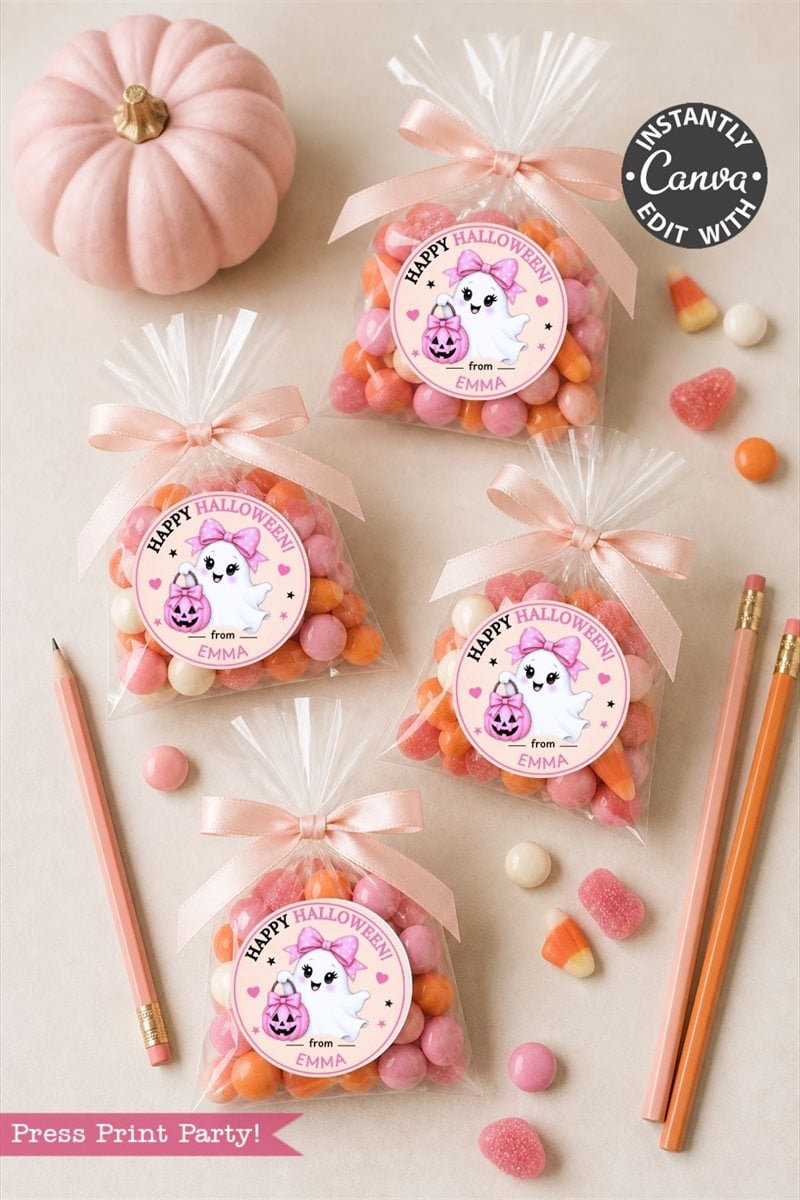 Four clear treat bags filled with pink and orange candies are each tagged with a Pink Coquette Halloween Ghost Round Label from the 6-pack set, featuring charming ghost and pumpkin designs that say “Happy Halloween.” Two pink pencils, assorted candy pieces, and a small pink pumpkin are arranged on a light surface.