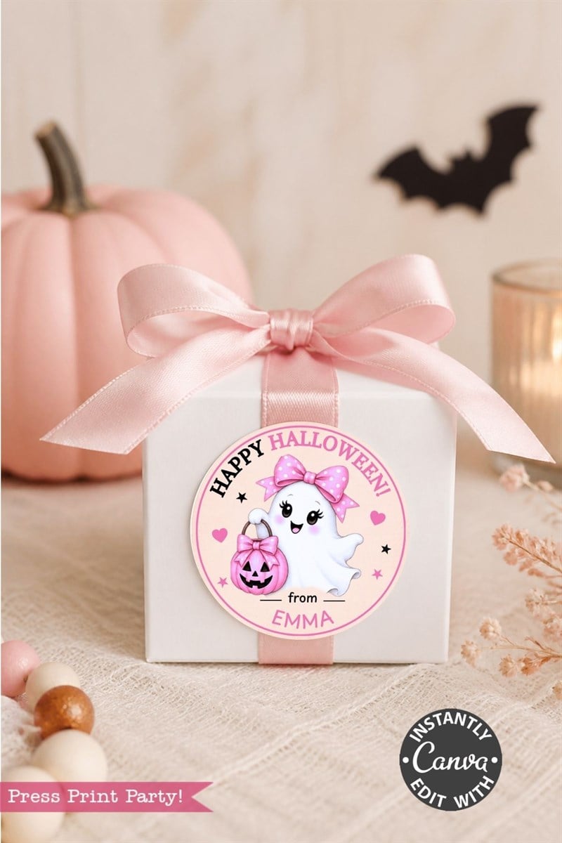 A white gift box with a pink ribbon is adorned with one of the 6 Pink Coquette Halloween Ghost Round Labels, featuring a cute ghost and the message “Happy Halloween from Emma.” The charming label adds a delightful touch, while a pink pumpkin and festive decor are seen in the background.
