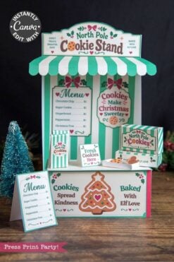 Festive North Pole cookie stand display with striped awning, cookie signs, menus, and cookie boxes featuring 6 Pink Coquette Halloween Ghost Round Labels, along with a small tree and gingerbread decorations on the table, promoting cookies “baked with elf love.”.