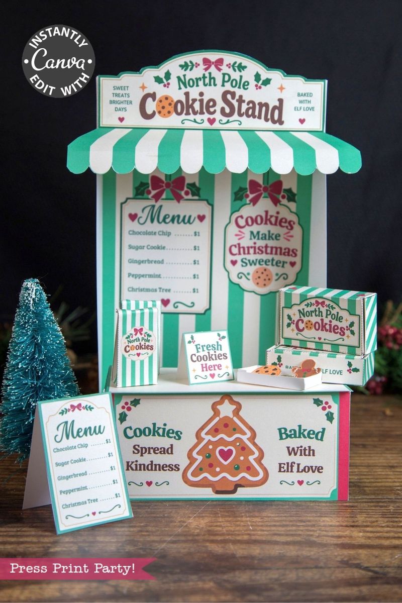 Festive North Pole cookie stand display with striped awning, cookie signs, menus, and cookie boxes featuring 6 Pink Coquette Halloween Ghost Round Labels, along with a small tree and gingerbread decorations on the table, promoting cookies “baked with elf love.”.