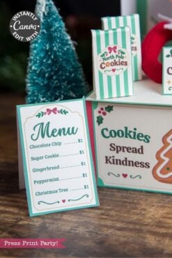 A festive cookie stand adorned with 6 Pink Coquette Halloween Ghost Round Labels, featuring a “Cookies Spread Kindness” sign, a menu listing various cookies for $1 each, and a small Christmas tree in the background.