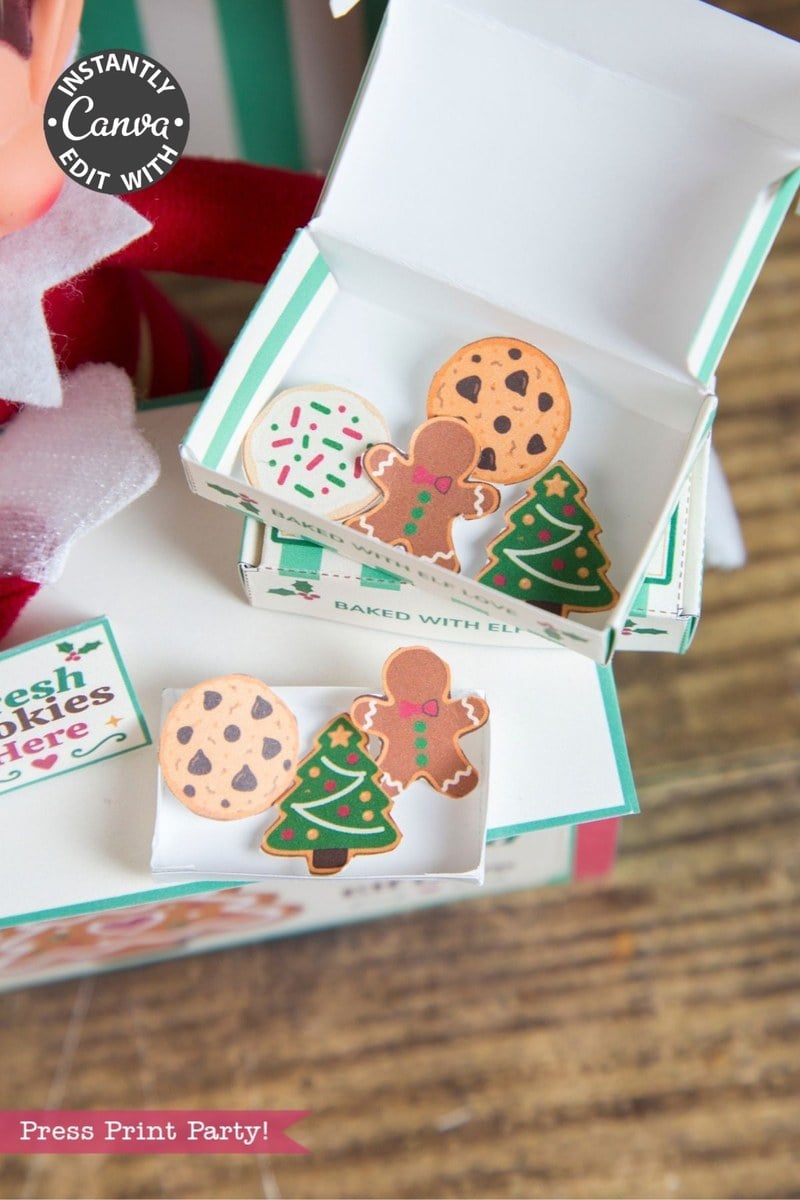 Small boxes with festive holiday cookie stickers, featuring a gingerbread man, Christmas tree, and chocolate chip cookies, rest on a wooden surface. In the background, 6 Pink Coquette Halloween Ghost Round Labels and a soft pink ribbon are partially visible, adding a charming touch to the scene.