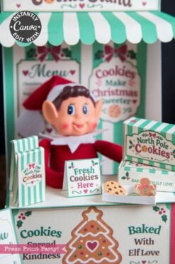 A smiling elf doll sits at a festive cookie stand with signs reading “Fresh Cookies Here” and “North Pole Cookies,” surrounded by decorated boxes adorned with 6 Pink Coquette Halloween Ghost Round Labels and Christmas-themed decorations.