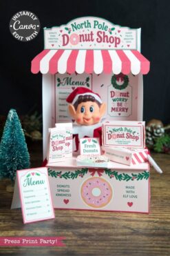 A festive North Pole Donut Shop display features an elf doll, donut menus, pink and green holiday decor, and mini donut boxes adorned with 6 Pink Coquette Halloween Ghost Round Labels, with a small tree beside the stand.