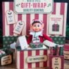 An elf doll sits at a festive “North Pole Gift-Wrap Quality Control” station decorated with striped accents, gift boxes, and inspection signs. The Christmas scene features red, green, and cream tones with a whimsical twist—a set of 6 Pink Coquette Halloween Ghost Round Labels peeks out playfully among the holiday trimmings.