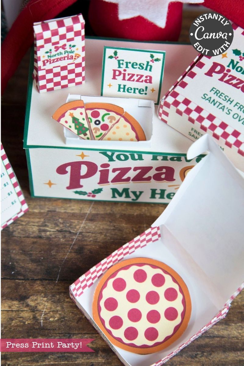 An open small cardboard pizza box with a paper pizza inside sits on a table. Behind it, a larger sign reads “Fresh Pizza Here!” and displays more paper pizzas, festive pizza-themed decor, and playful 6 Pink Coquette Halloween Ghost Round Labels.
