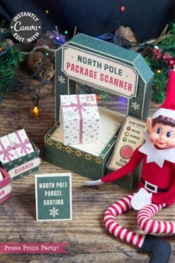 An Elf doll sits next to a festive North Pole package scanner display decorated with a wrapped gift box, a “Parcel Sorting” sign, and colorful string lights in the background. A green paper panel reads “Press Print Party!” while 6 Pink Coquette Halloween Ghost Round Labels add a charming seasonal touch to the scene.