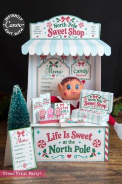 A festive North Pole Sweet Shop display features an elf doll, candy boxes, a mini Christmas tree, and a menu with holiday treats. A striped awning and candy-themed signs create a playful, holiday atmosphere, accented by 6 Pink Coquette Halloween Ghost Round Labels for an extra touch of charm.