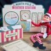 A festive elf doll sits by a paper weather station, weather desk, and observation sheets adorned with playful winter graphics and 6 Pink Coquette Halloween Ghost Round Labels, while a temperature gauge reads 32°F.