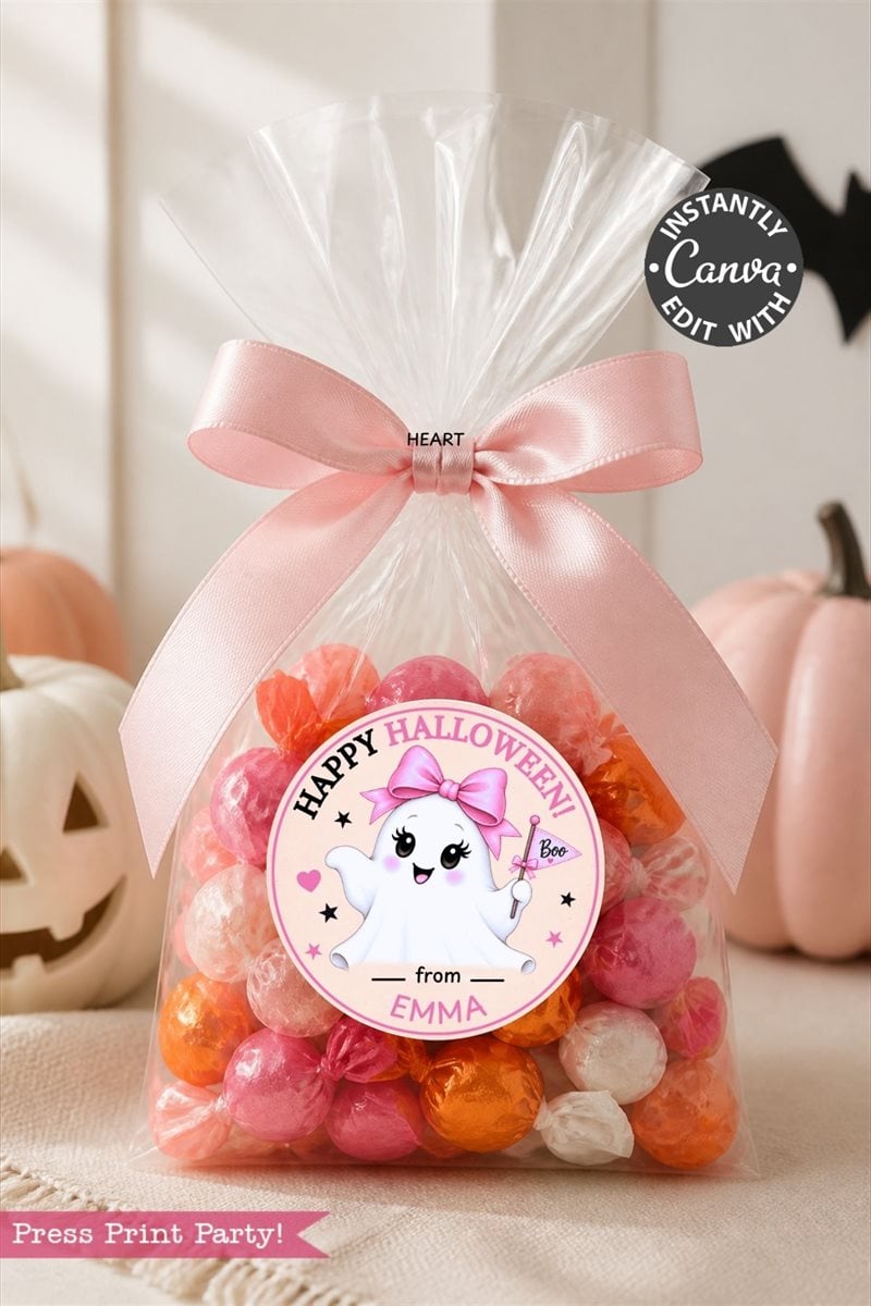 A clear bag of orange, pink, and white candies with a pink bow is topped with a ghost-themed label from the 6 Pink Coquette Halloween Ghost Round Labels set that reads “Happy Halloween from Emma.” White pumpkins decorate the background.