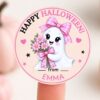 A cute ghost with a pink bow holds flowers on a round sticker that reads “Happy Halloween! from EMMA.” The design features the 6 Pink Coquette Halloween Ghost Round Labels, which have a pink border and star accents, and the label sits on a fingertip. “Press Print Party!” appears at the bottom.