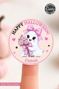 A cute ghost with a pink bow holds flowers on a round sticker that reads “Happy Halloween! from EMMA.” The design features the 6 Pink Coquette Halloween Ghost Round Labels, which have a pink border and star accents, and the label sits on a fingertip. “Press Print Party!” appears at the bottom.
