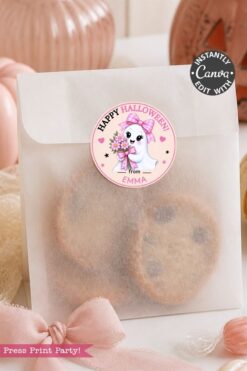 A translucent treat bag filled with cookies, sealed with a 6 Pink Coquette Halloween Ghost Round Label—a pink “Happy Halloween” sticker featuring a cute ghost holding flowers and the message “from Emma.” Pink decorations are arranged nearby.