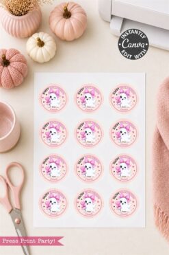 A sheet of six Pink Coquette Halloween Ghost round labels with cute ghost and pink decorations is surrounded by pastel pumpkins, scissors, a cup, and a printer on a light desk.