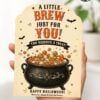 A hand holds one of the 7 Vintage Halloween Gift Card Holders, featuring a cauldron filled with colorful balls, bats, and stars. The card is perfect for holding Halloween gift cards and reads: “A little brew just for you! You deserve a treat! Happy Halloween!”.
