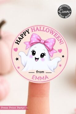 A round pink sticker from the 6 Pink Coquette Halloween Ghost Round Labels collection showcases a cute smiling ghost wearing a pink polka-dot bow with the text “Happy Halloween! from EMMA.” The sticker is displayed on a fingertip, with softly blurred pumpkins in the background.