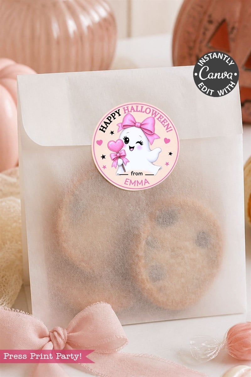 A frosted bag of cookies is sealed with one of the 6 Pink Coquette Halloween Ghost Round Labels, which features a cute ghost, a bow, and the message “Happy Halloween from Emma.” The scene is decorated with pink accents and pumpkins in the background.