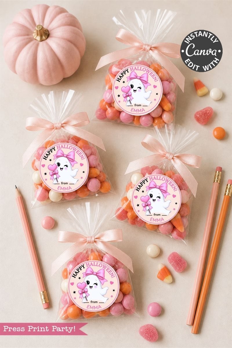 Four clear treat bags filled with pink, orange, and white candies—each tied with a ribbon and decorated using Pink Coquette Halloween Ghost Round Labels from a pack of six reading “Happy Halloween”—are arranged alongside pencils and candy on a beige surface. A small pink pumpkin sits nearby.