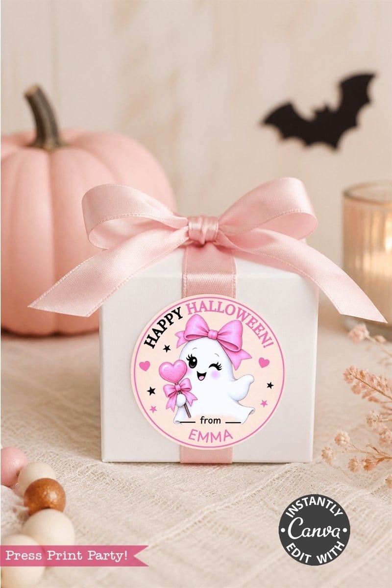 A white gift box with a pink ribbon sits in front of a pink pumpkin. The box is decorated with one of our 6 Pink Coquette Halloween Ghost Round Labels—a “Happy Halloween” tag featuring a cute ghost holding a pink bow and personalized with the name “Emma” at the bottom.