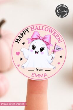 A sticker on a fingertip shows a cute ghost with a pink bow and a “Boo” flag, with the text “Happy Halloween! From Emma.” Pink pumpkins are blurred in the background.