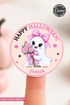 A round sticker with a cute ghost holding flowers and wearing a pink bow, reading “Happy Halloween! from EMMA.” The sticker has pink accents and stars, and is displayed on a finger.