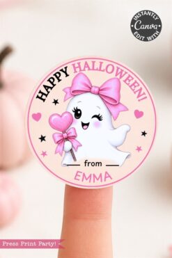 A circular Halloween sticker features a smiling ghost with pink bows and a heart wand, and the text “Happy Halloween! from Emma.” The sticker is held on a fingertip.