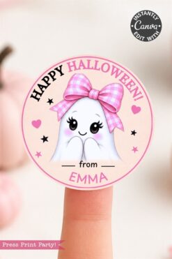 A round sticker with a cute ghost wearing a pink bow, text reads “Happy Halloween! from EMMA,” and pink stars around. Held on a fingertip, with a soft pink background.