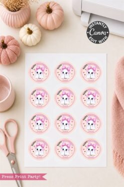 A sheet of round “Happy Halloween” stickers with a cute dog in a unicorn costume, surrounded by pink decor, pumpkins, scissors, a cup, and a cozy pink cloth on a light surface.