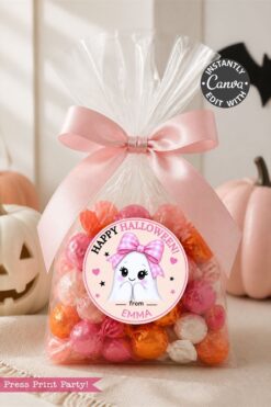 A clear bag filled with pink, orange, and white candies is tied with a pink ribbon and adorned with one of the 6 Pink Coquette Halloween Ghost Round Labels reading “Happy Halloween from Emma”; the bag sits surrounded by pumpkins.