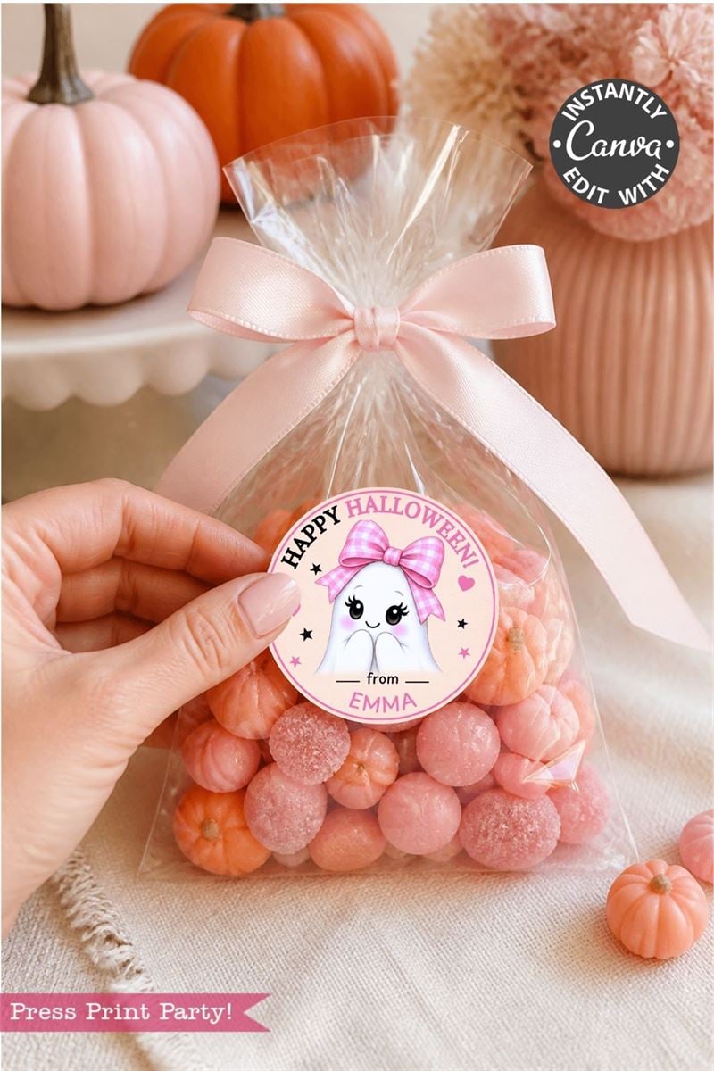 A hand holds a clear bag of pink candies tied with a pale pink ribbon and finished with one of the 6 Pink Coquette Halloween Ghost Round Labels, featuring a cute ghost and “Happy Halloween from Emma.” Pink pumpkins and festive decor are seen in the background.
