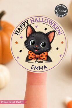 A finger holds a round sticker with a cute black cat in an orange polka dot bow tie, stars, “Happy Halloween!” text, and “from Emma.” Pumpkins are blurred in the background.