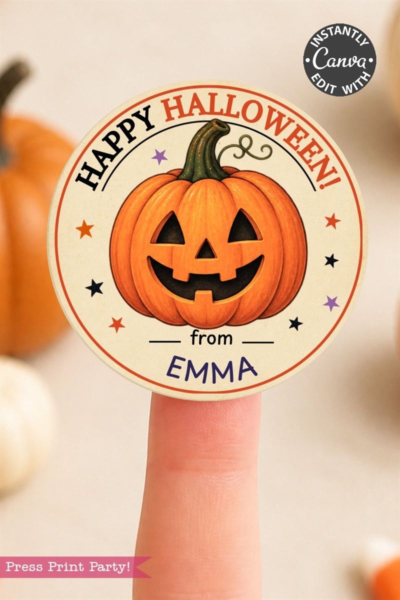 A finger holds a round Halloween sticker featuring a smiling jack-o’-lantern and the text “Happy Halloween! from Emma.” A pumpkin and blurred objects are in the background.