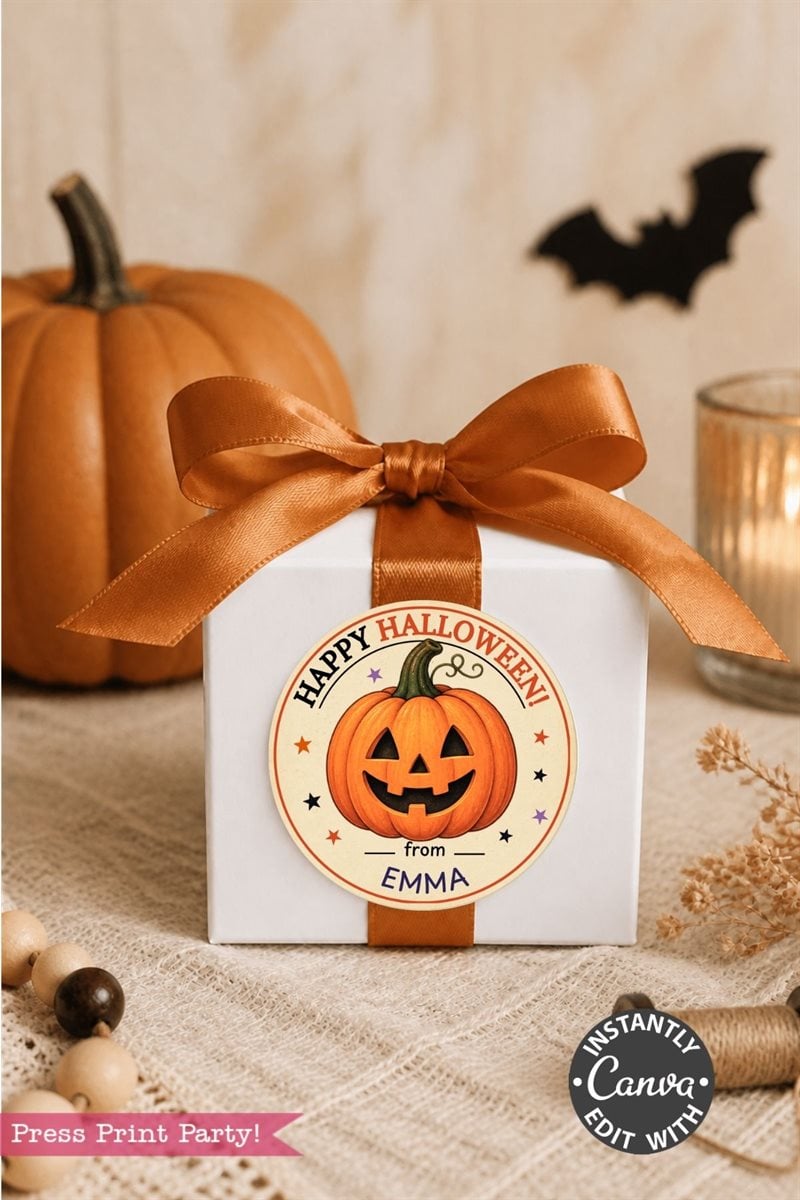 A white gift box with an orange ribbon, featuring a round Halloween sticker with a jack-o’-lantern, stars, and “Happy Halloween from EMMA.” A pumpkin, candle, and autumn decor are in the background.