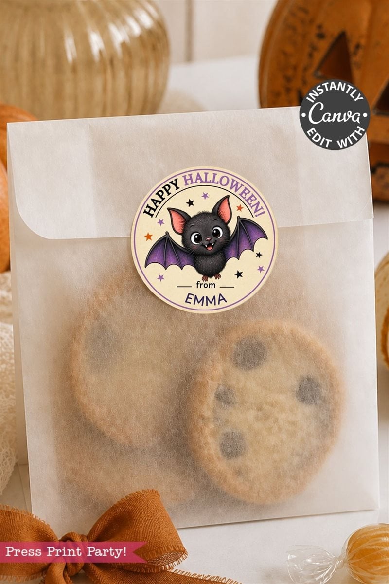 A clear bag filled with chocolate chip cookies is sealed with a Pink Coquette Ghost Treat Bag Halloween Sticker, which features a cute bat and the text “Happy Halloween from Emma.” In the background, there is a pumpkin and ribbon.