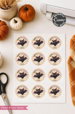 A sheet of Pink Coquette Ghost Treat Bag Halloween Stickers sits on a table alongside scissors, pumpkins, a printer, and an orange plaid cloth. The round pink stickers read “Happy Halloween” and feature adorable cartoon bats.