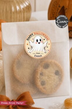 A translucent bag filled with cookies is sealed using the Pink Coquette Ghost Treat Bag Halloween Stickers, which feature a round pink design with a smiling ghost and the text “Happy Halloween from Emma.” Autumn decor is seen in the background.