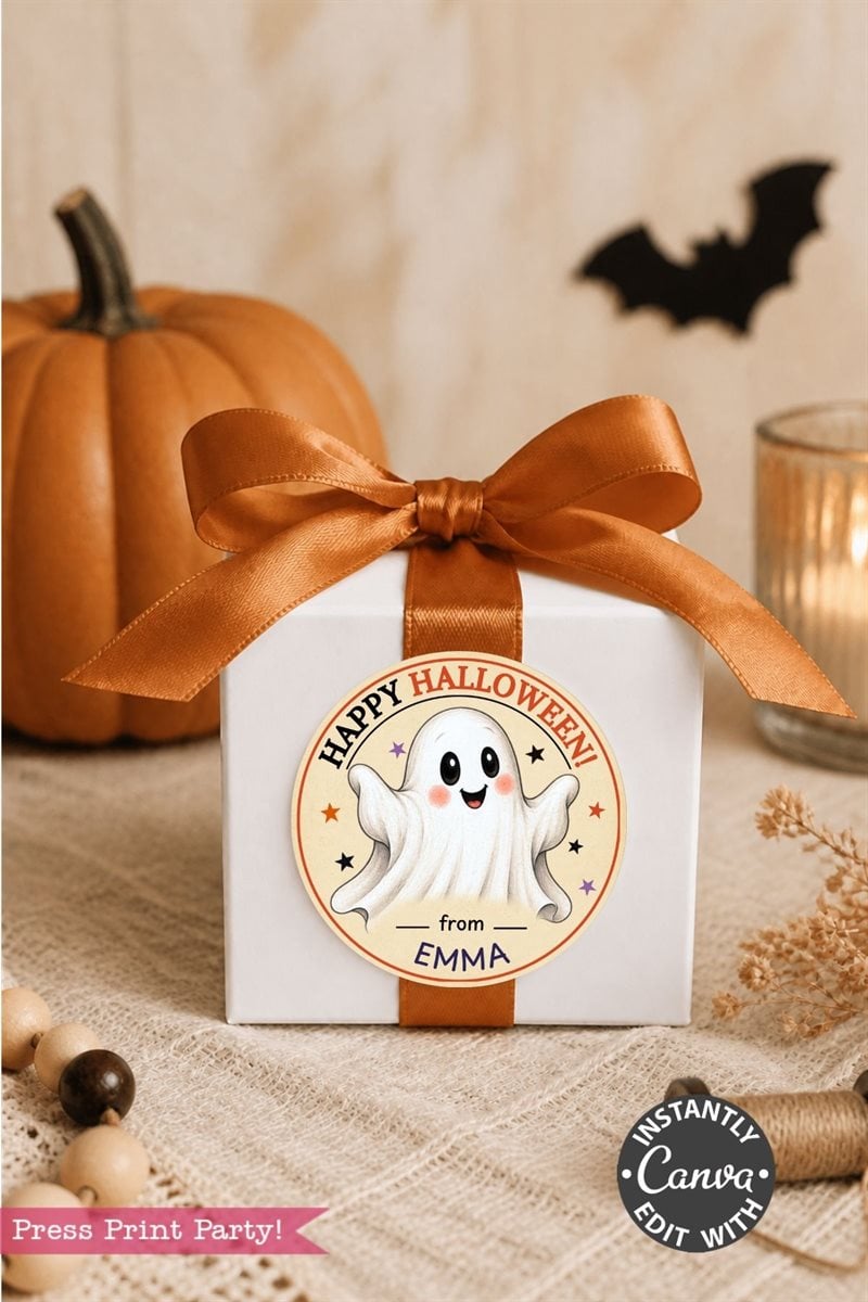 A white gift box with an orange ribbon is decorated with a round label featuring a cute ghost and the message “Happy Halloween from Emma,” accented by Pink Coquette Ghost Treat Bag Halloween Stickers. A pumpkin and candle rest in the background on a beige surface.