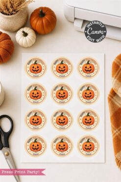 A sheet of Pink Coquette Ghost Treat Bag Halloween Stickers, featuring round, pink stickers with smiling jack-o’-lanterns and “Happy Halloween” messages, sits on a table alongside scissors, pumpkins, a plaid cloth, and a printer. The stickers are customizable in Canva.